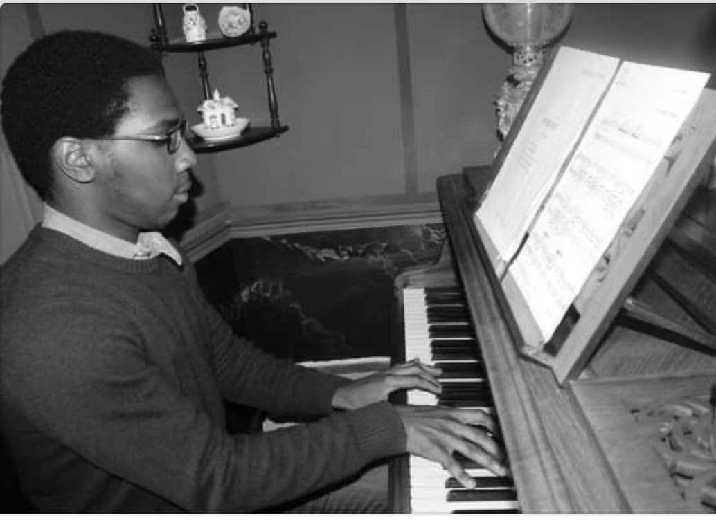 Trevor playing a wooden upright piano in a blue-walled room